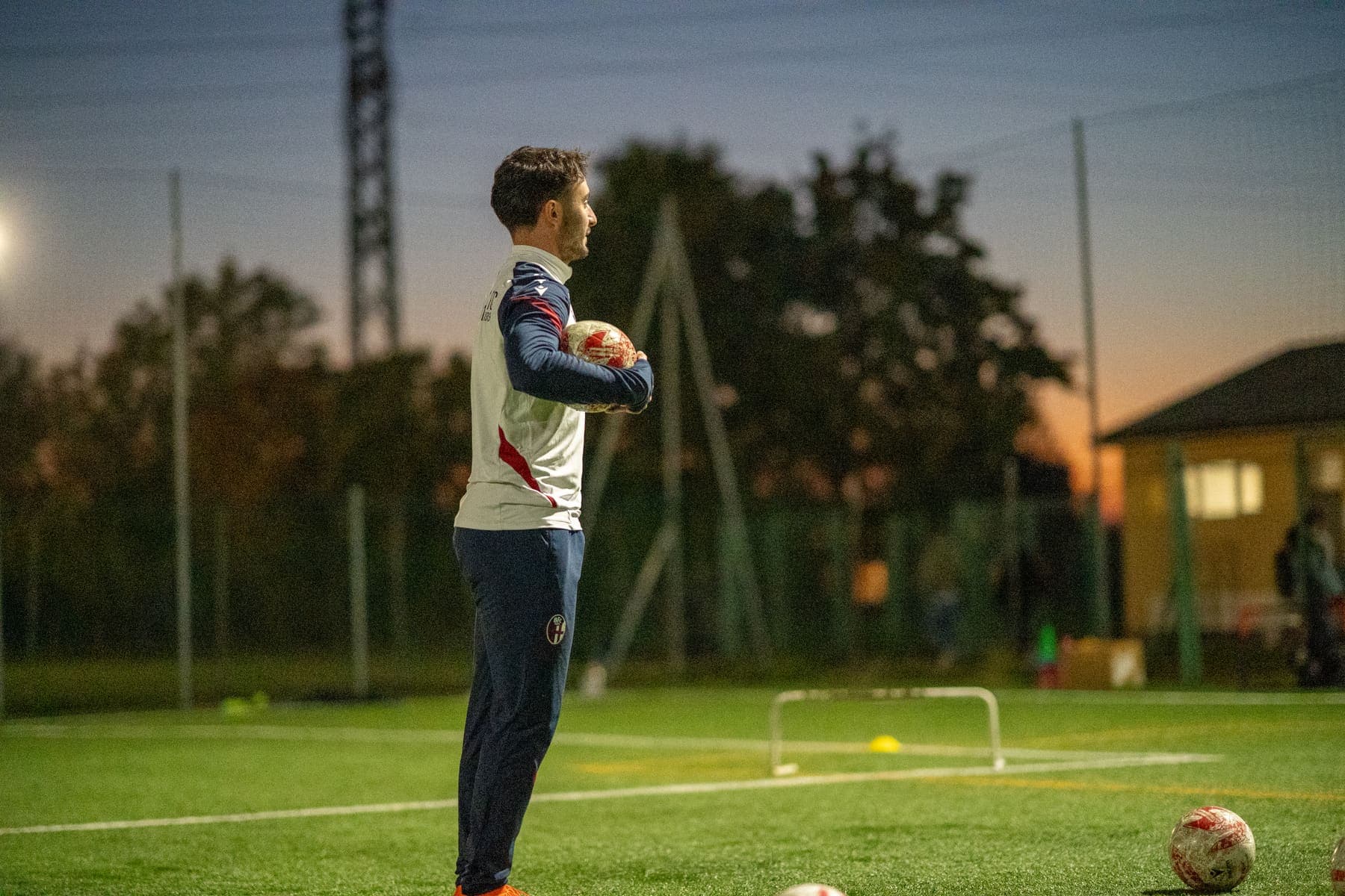 Ein Trainer des Bologna FC 1909 mit Ball im Abendlicht auf dem Trainingsplatz